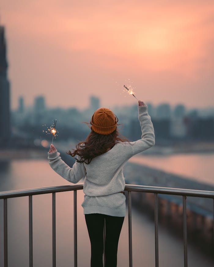 who-we-are A young woman celebrates with sparklers on a balcony overlooking Seoul during a winter sunset.